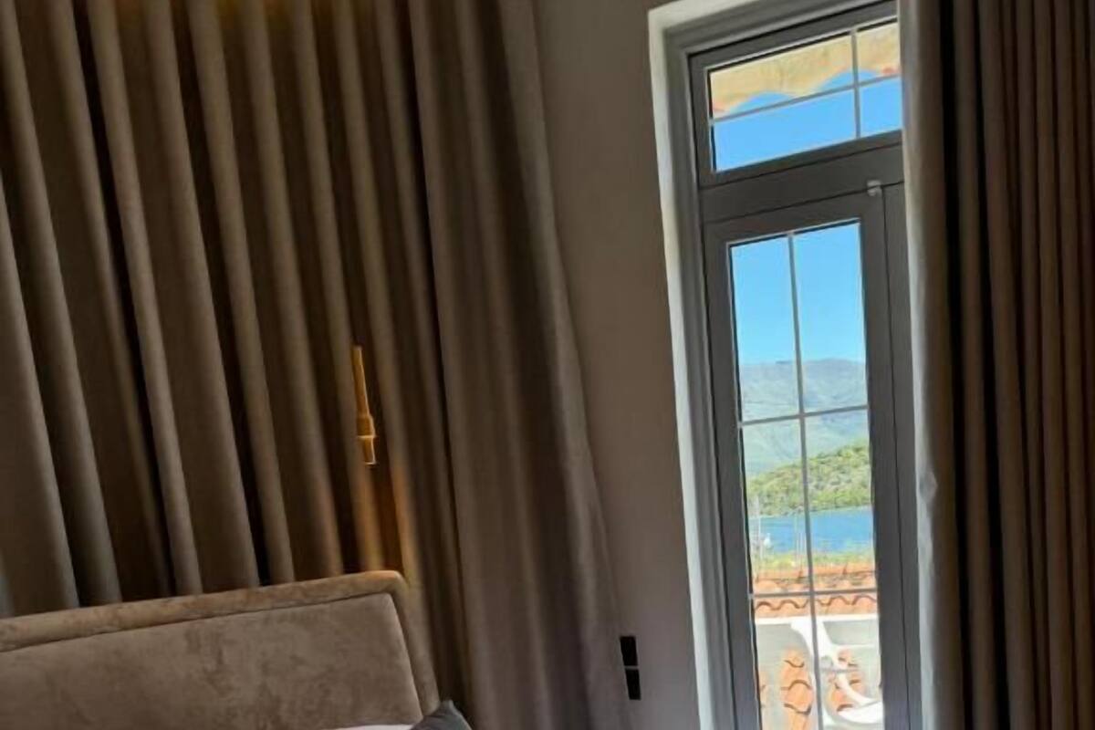 A hotel room with a large bed, a headboard, and a view of a mountainous landscape through a large window.