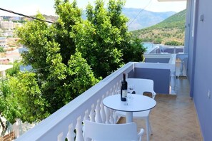 A balcony with a table and chairs, a bottle of wine, and a view of greenery and buildings. - Villa CACA (Ksamil)