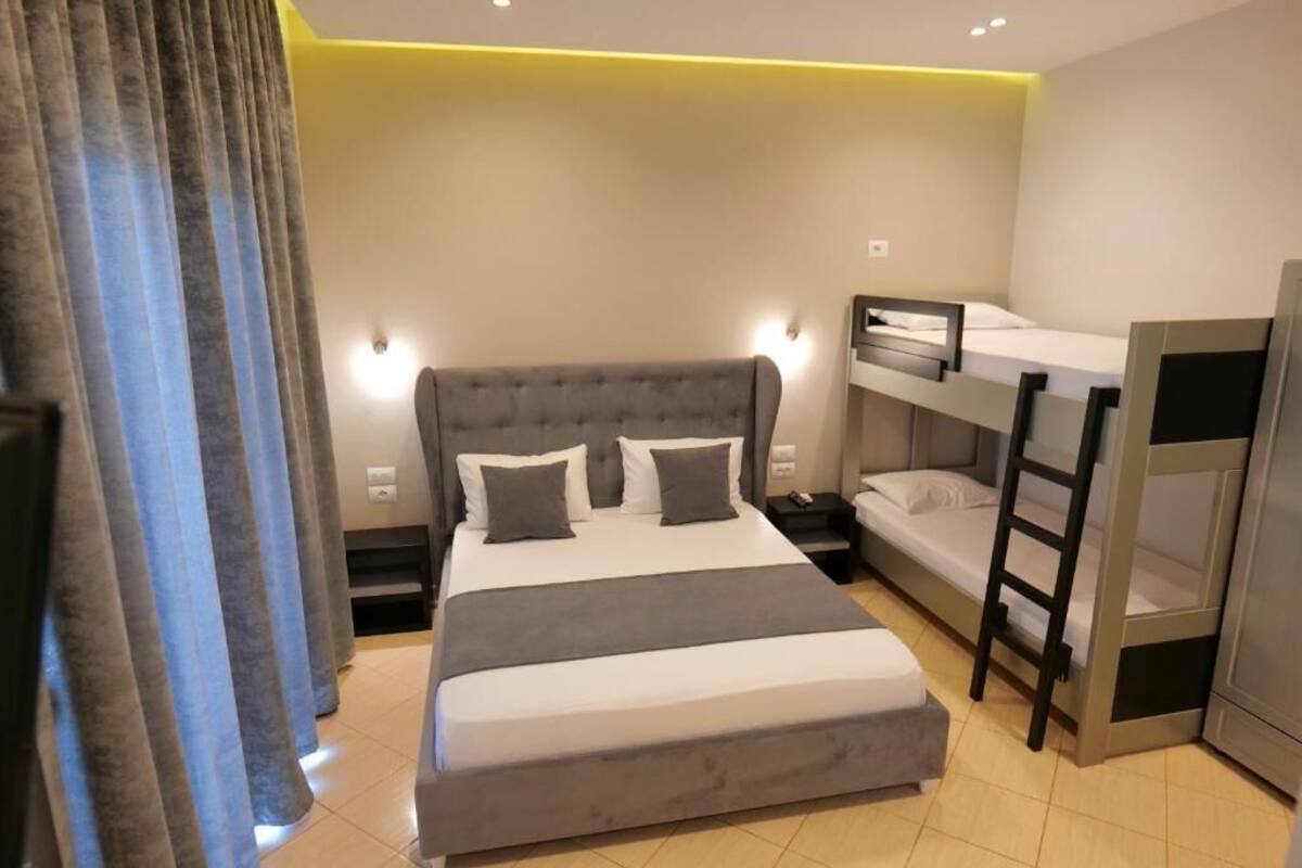 A modern hotel room with a large bed, a bunk bed, a desk, and a wardrobe.