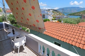 A balcony with a table and chairs, a view of a red-tiled roof, and a body of water in the background. - Villa CACA (Ksamil)