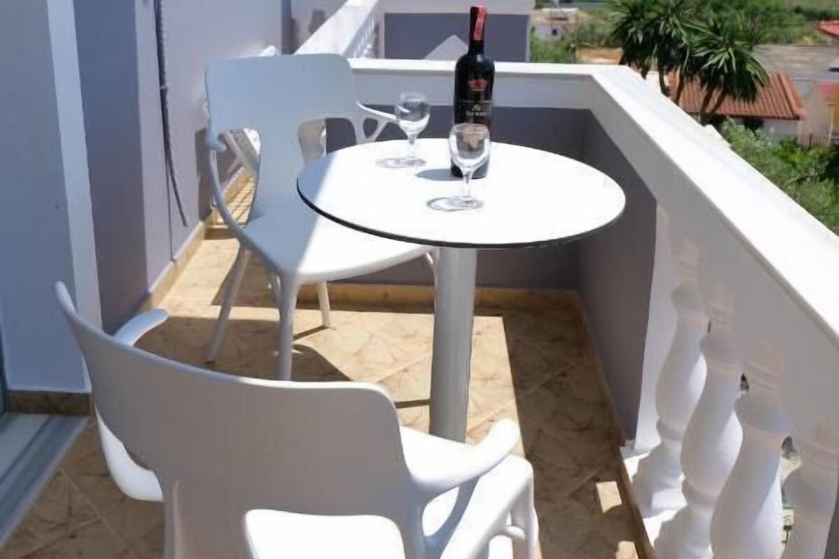 A balcony with a round table and two white chairs, a bottle of wine, and a glass on the table.