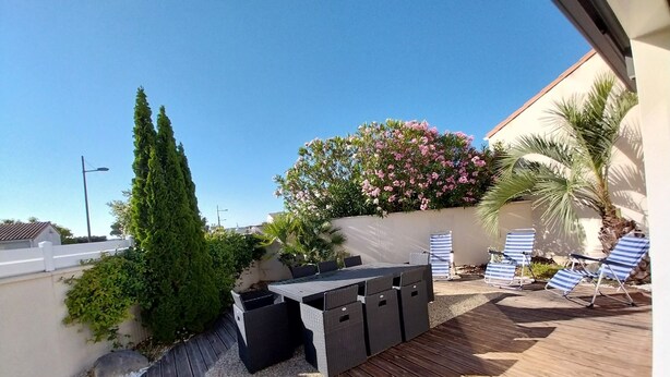 Eine Terrasse mit Holzboden, Tisch und Stühlen sowie einem Blumenstrauch.