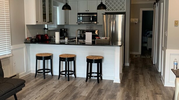 Una cocina moderna con una isla central, taburetes de bar, ventilador de techo y un refrigerador de acero inoxidable.