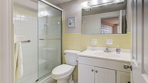 A bathroom with a glass-enclosed shower, a toilet, a sink with a mirror above, and a towel rack. - Directly on the Gulf - Unit  1 - 3 Bedroom - Ground Floor - Sleeps 6 (Venice)