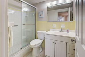 Un baño con ducha de vidrio, inodoro, lavamanos con espejo y toallero.