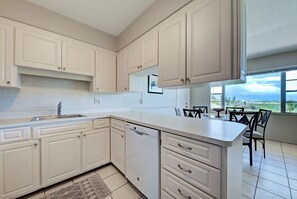 A modern kitchen with white cabinetry, a built-in dishwasher, and a dining area with a table and chairs. - Directly on the Gulf - Unit  1 - 3 Bedroom - Ground Floor - Sleeps 6 (Venice)