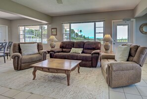 A living room with a brown leather sofa, two armchairs, a wooden coffee table, and a patterned rug. - Directly on the Gulf - Unit  1 - 3 Bedroom - Ground Floor - Sleeps 6 (Venice)