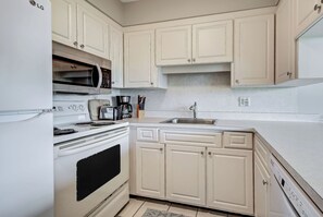 Una cocina con gabinetes blancos, microondas, estufa, cafetera y pileta.