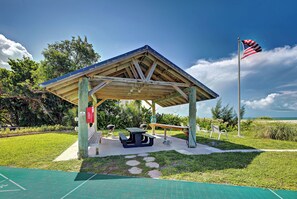 A covered picnic area with a bench, picnic table, and grill, surrounded by grass and trees. - Directly on the Gulf - Unit  1 - 3 Bedroom - Ground Floor - Sleeps 6 (Venice)