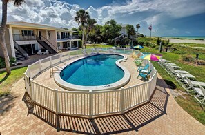 A swimming pool with a wooden deck and a white fence, surrounded by chairs and umbrellas. - Directly on the Gulf - Unit  1 - 3 Bedroom - Ground Floor - Sleeps 6 (Venice)