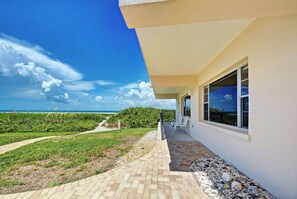 A pathway leading to a building with a view of the ocean, a patio area with chairs, and a well-maintained garden. - Directly on the Gulf - Unit  1 - 3 Bedroom - Ground Floor - Sleeps 6 (Venice)