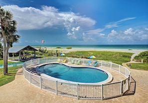 A pool with a white fence, a beach view, and a flag.
