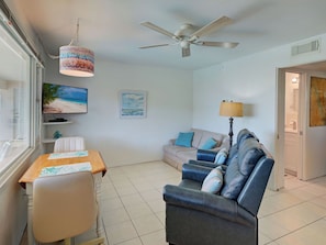 A living room with a TV, a ceiling fan, a sofa, and a dining table. - Directly on the Gulf - Unit 13 - 1 Bedroom - Second Floor - Sleeps up to 4 (Venice)