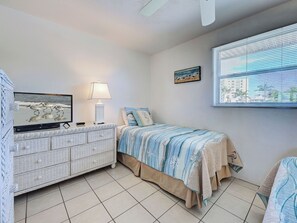 A bedroom with a bed, a dresser, a lamp, a painting, and a window with blinds. - Directly on the Gulf - Unit 13 - 1 Bedroom - Second Floor - Sleeps up to 4 (Venice)