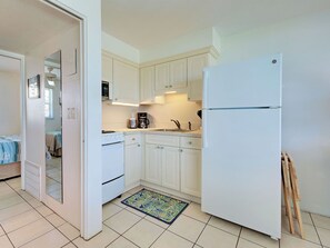 A compact kitchen with white cabinets, a built-in oven, a refrigerator, and a coffee maker. - Directly on the Gulf - Unit 13 - 1 Bedroom - Second Floor - Sleeps up to 4 (Venice)