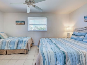 A bedroom with two beds, a ceiling fan, a window with blinds, a painting on the wall, and a lamp on the nightstand. - Directly on the Gulf - Unit 13 - 1 Bedroom - Second Floor - Sleeps up to 4 (Venice)