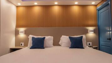 A hotel room with a bed, two bedside tables, a nightstand, a blue wardrobe, and a ceiling with recessed lighting.