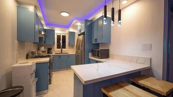 A modern kitchen with blue cabinets, a marble island, and pendant lighting.
