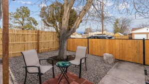 Une terrasse avec deux chaises et une table, entourée d’une clôture en bois et d’un arbre.