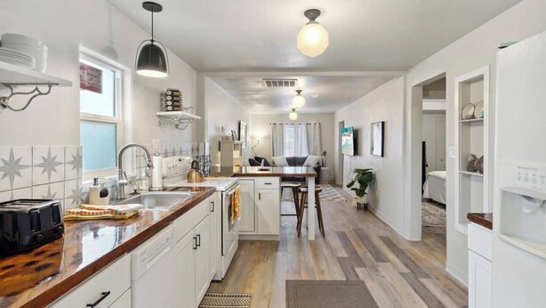 Une cuisine moderne avec des meubles blancs, un plan de travail en bois et un coin repas comprenant une table et des chaises.