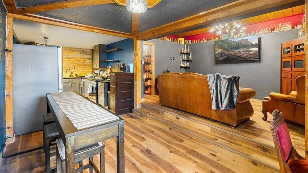 A cozy living room with a wooden floor, a sofa, a table, and a kitchen area with a refrigerator and cabinets. - The Bizarre and the Beautiful (Albuquerque)