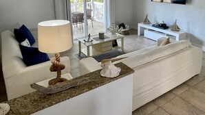 Ein modernes Wohnzimmer mit einem weißen Sofa, einem Couchtisch, einem an der Wand befestigten Fernseher und einem Deckenventilator.