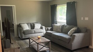 Ein Wohnzimmer mit zwei grauen Sofas, einem Holztisch und einem Fernsehschrank.
