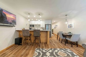 A modern kitchen with a central island, wooden flooring, and a dining area with a table and chairs.