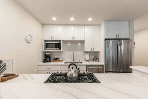 A modern kitchen with white cabinets, a stainless steel refrigerator, a microwave, and a gas stove.