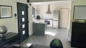 A modern kitchen with a central island, a dining area with a table and chairs, and a black door with a globe on top. - Maison 2 à 8 Personnes Plurien - Sables D'or les Pins, à 800 m de la Plage (Plurien)