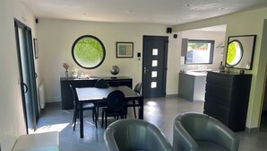 A modern living room with a dining area, featuring a black dining table, two black chairs, a white ottoman, and a black sofa. - Maison 2 à 8 Personnes Plurien - Sables D'or les Pins, à 800 m de la Plage (Plurien)