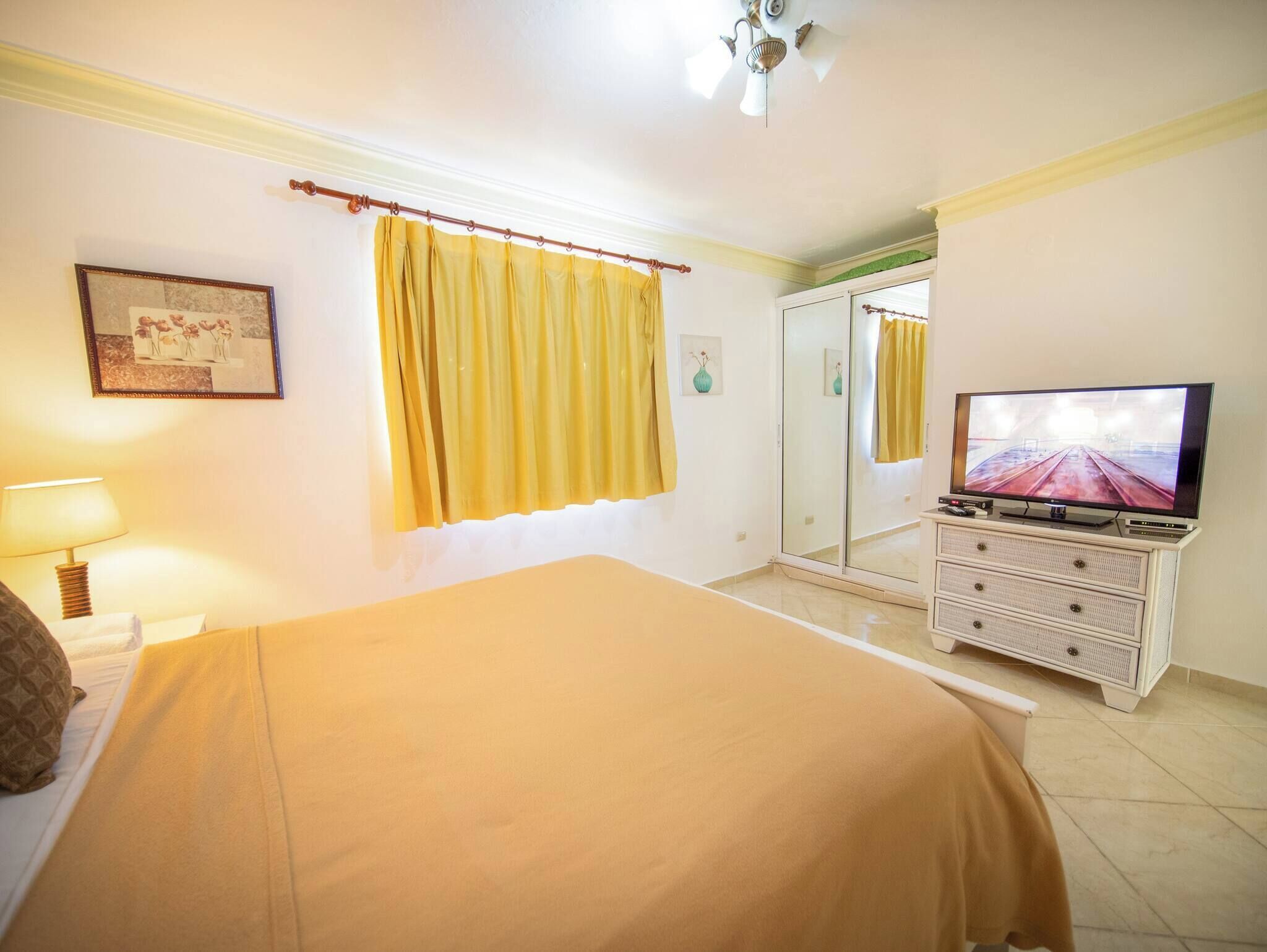 A hotel room with a bed, a television, a mirror, and a window with curtains.