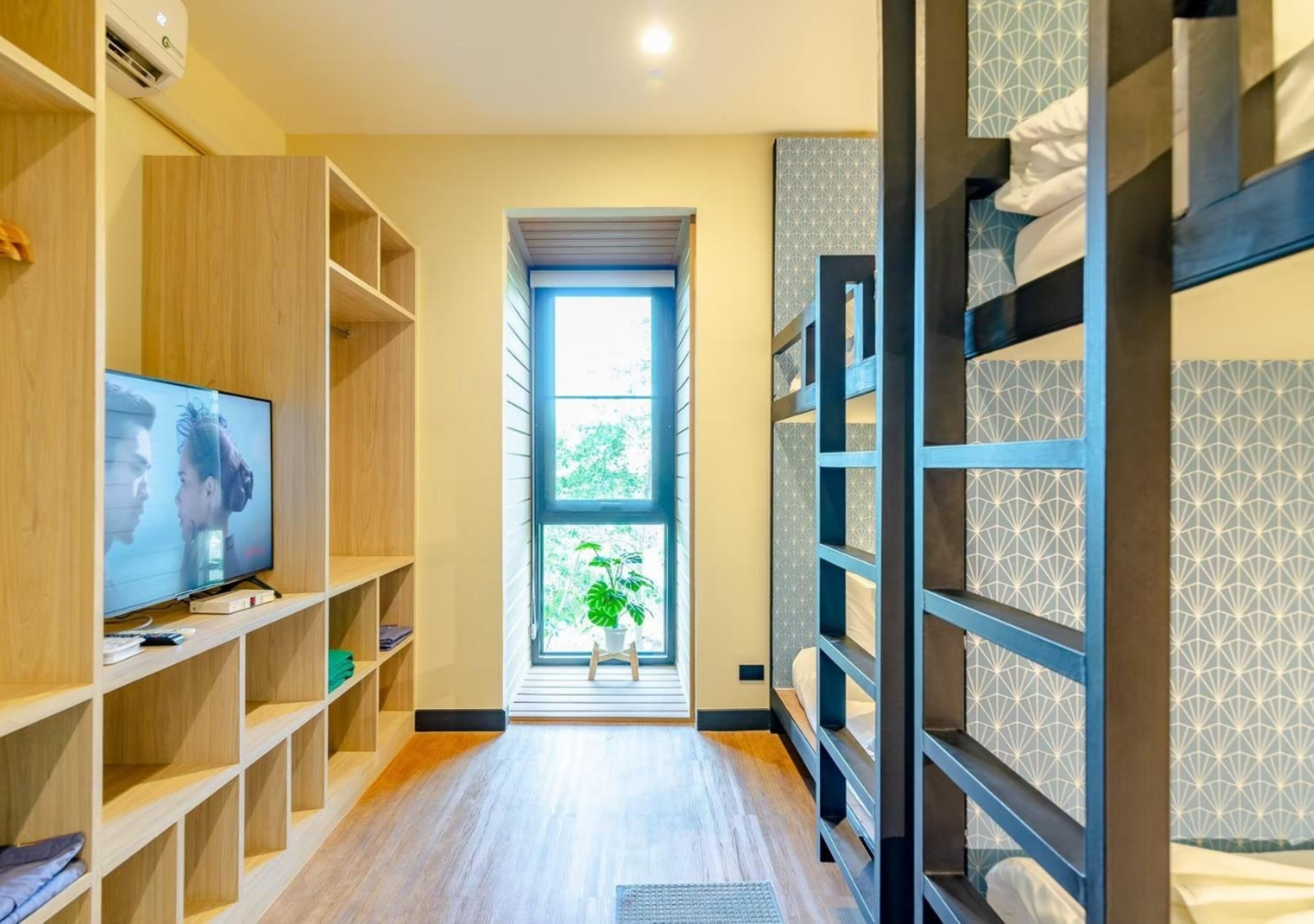 Habitación de hotel con literas, televisión, estanterías de madera, ventana con vistas a zonas verdes y pared con diseño.