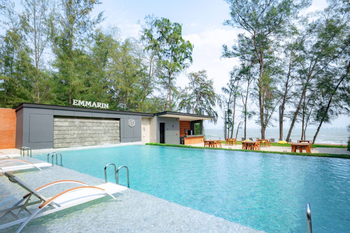 A pool area with lounge chairs, a bar, and a view of the ocean.