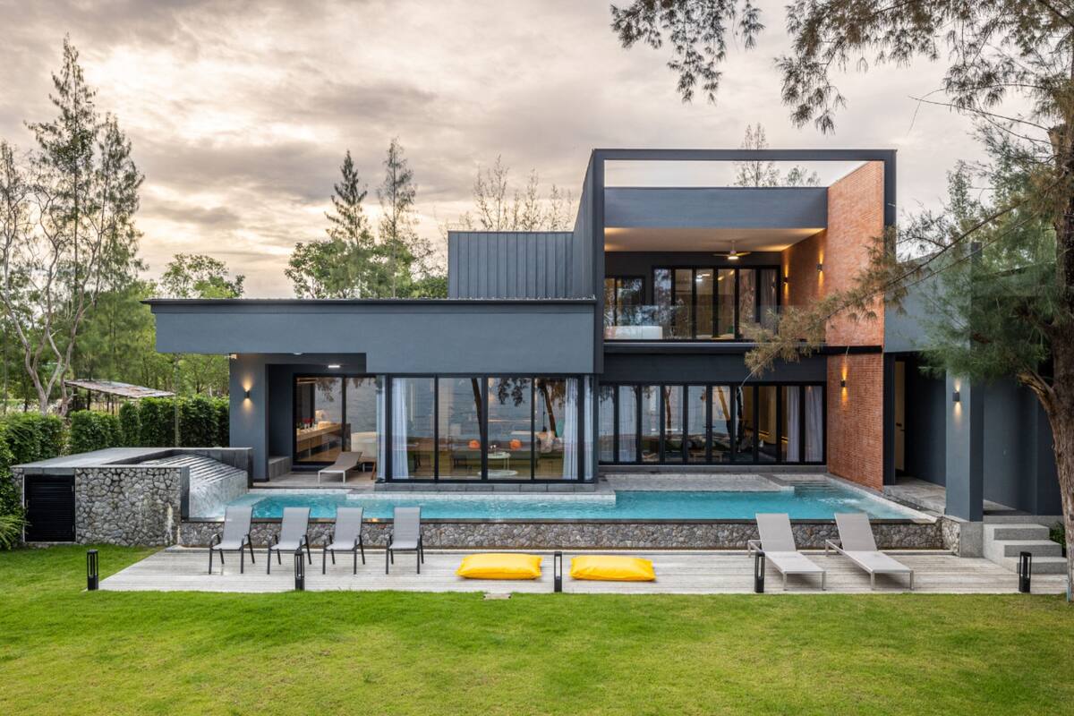 A modern two-story house with a swimming pool, outdoor seating, and a stone wall.
