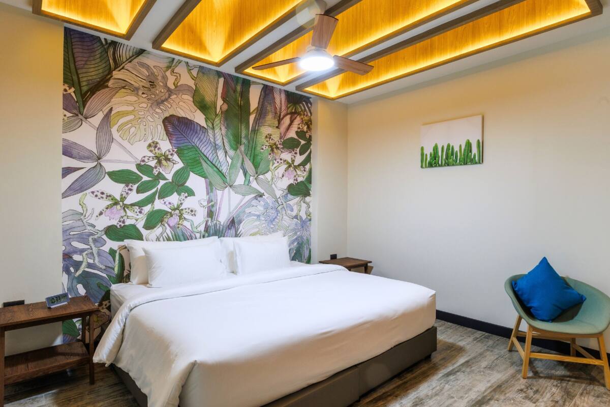 A bedroom with a large bed, a ceiling fan, a nightstand, a chair, and a wall mural.