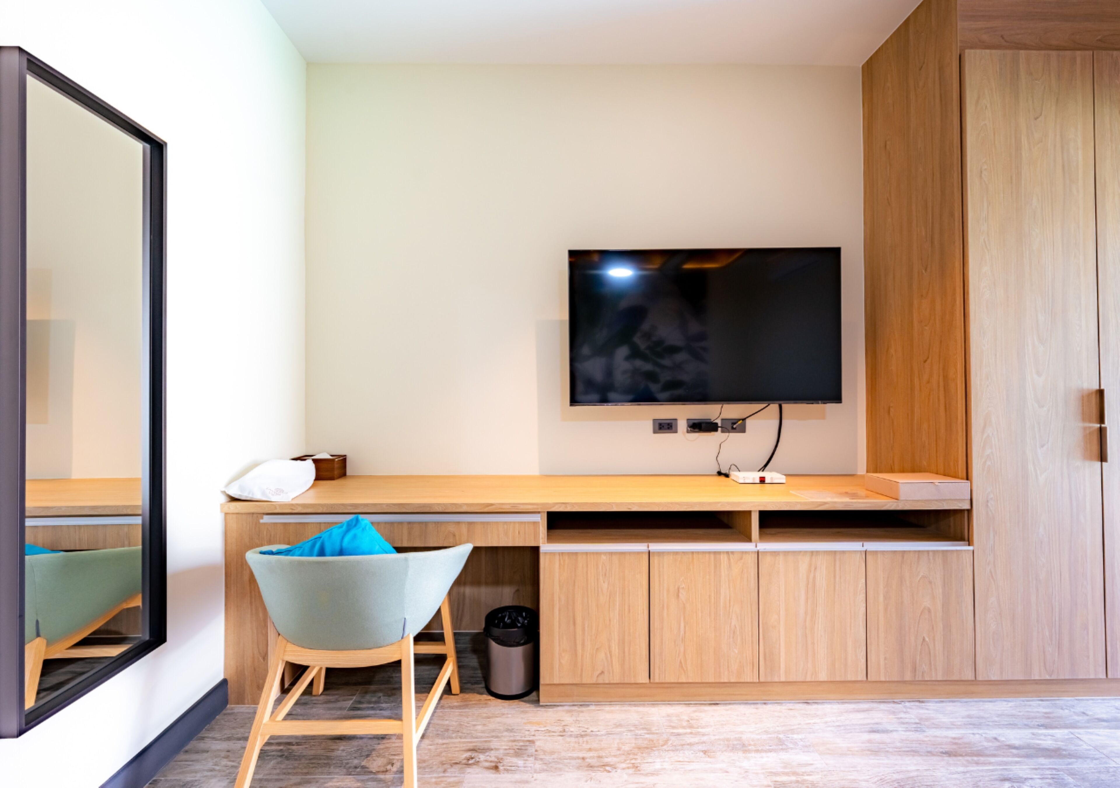 A modern room with a wooden desk, a chair, a television mounted on the wall, and a wardrobe.