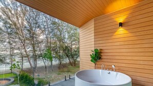 Un baño moderno con una bañera independiente grande, paneles de madera y vistas a un jardín ajardinado.
