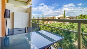 Ein Balkon mit Glastisch und Stühlen, mit Blick auf ein Wohngebiet mit Bäumen und Gebäuden.