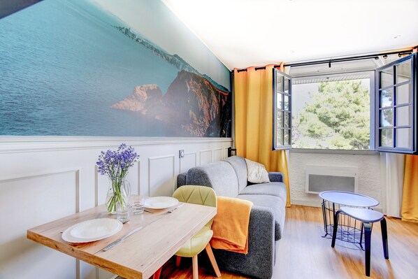 A cozy room with a dining table, a sofa, and a view of the sea through a large window.