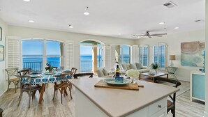 A spacious dining area with a view of the ocean, a ceiling fan, and a table set with plates and a bottle. - ☀️Beachfront 30A Penthouse with Incredible Views-Endless Sea☀️ (Santa Rosa Beach)