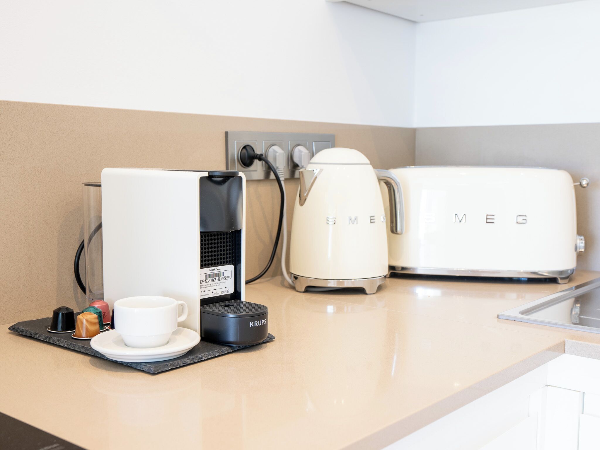 A kitchenette with a coffee maker, a toaster, and a cup on a black mat.
