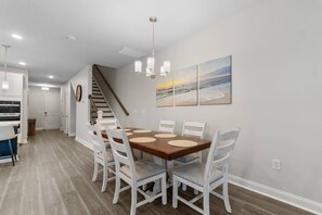 Un coin repas avec une table en bois et des chaises blanches, un escalier et un tableau accroché au mur.