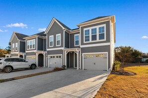 A two-story residential building with a garage, driveway, and a parked car. - Driving range views | 3BR townhome | Resort pools (North Myrtle Beach)