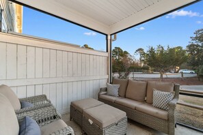 A covered outdoor seating area with wicker furniture, a cushioned sofa, and a view of a street and trees.