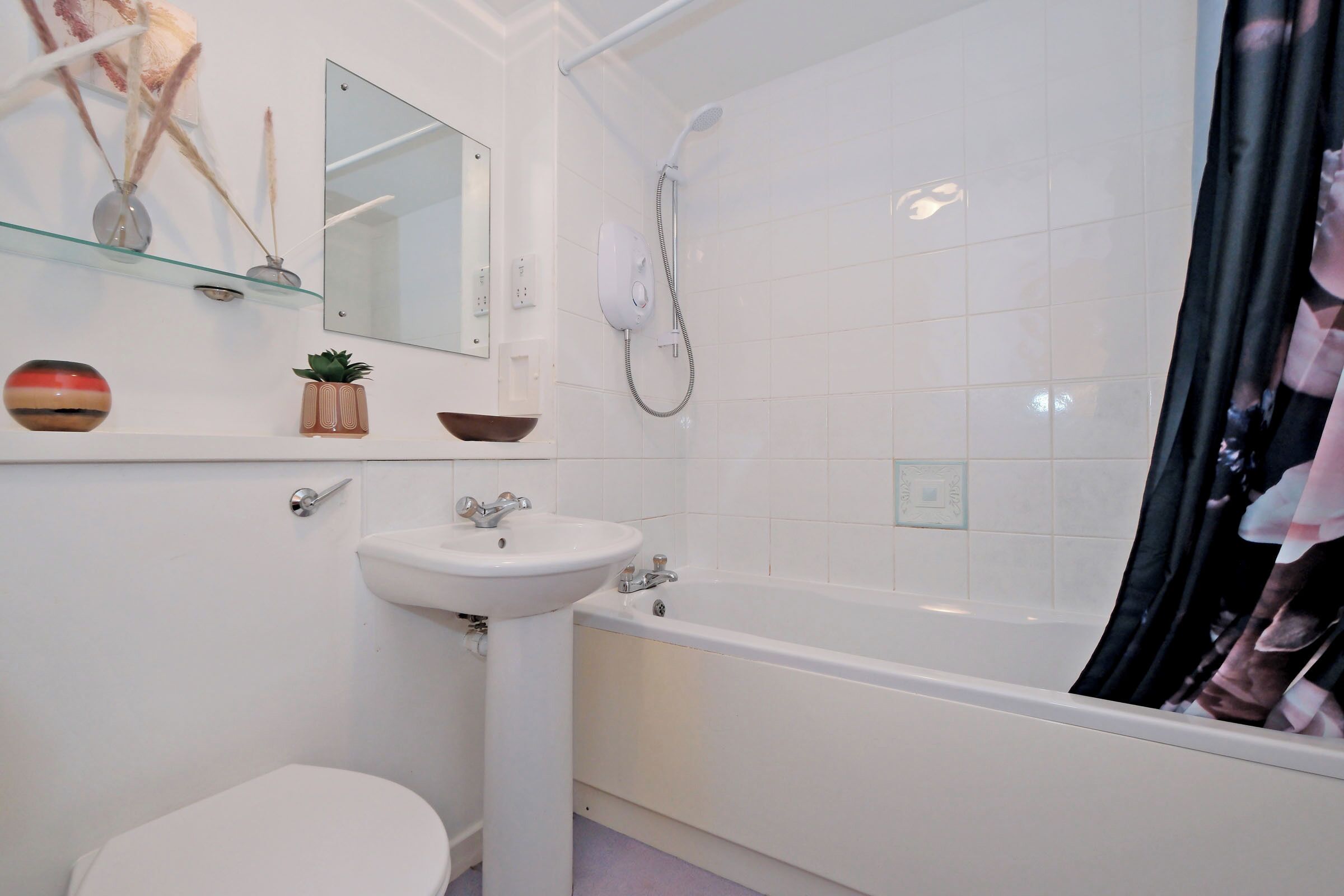A bathroom with a white sink, toilet, and bathtub. There is a mirror above the sink and a showerhead above the bathtub.