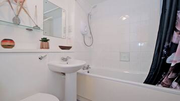 A bathroom with a white sink, toilet, and bathtub. There is a mirror above the sink and a showerhead above the bathtub.