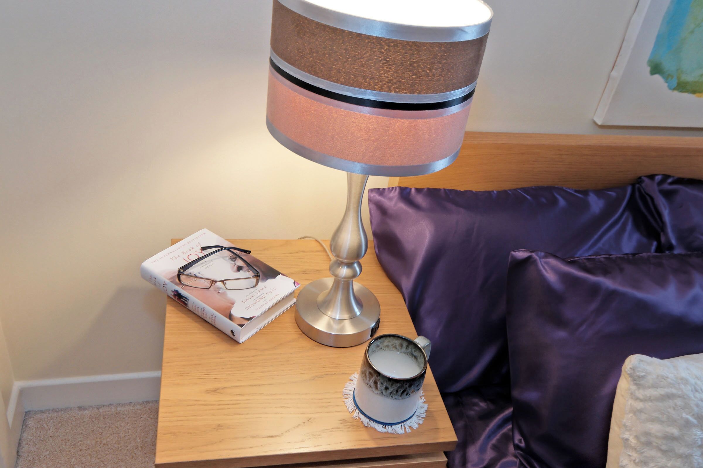 A bedside table with a lamp, a book, and a mug.