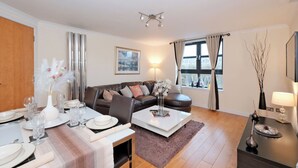 Ein modernes Wohnzimmer mit Essbereich, einer Sofagarnitur, einem Couchtisch und Blick auf die Stadt durch das Fenster.