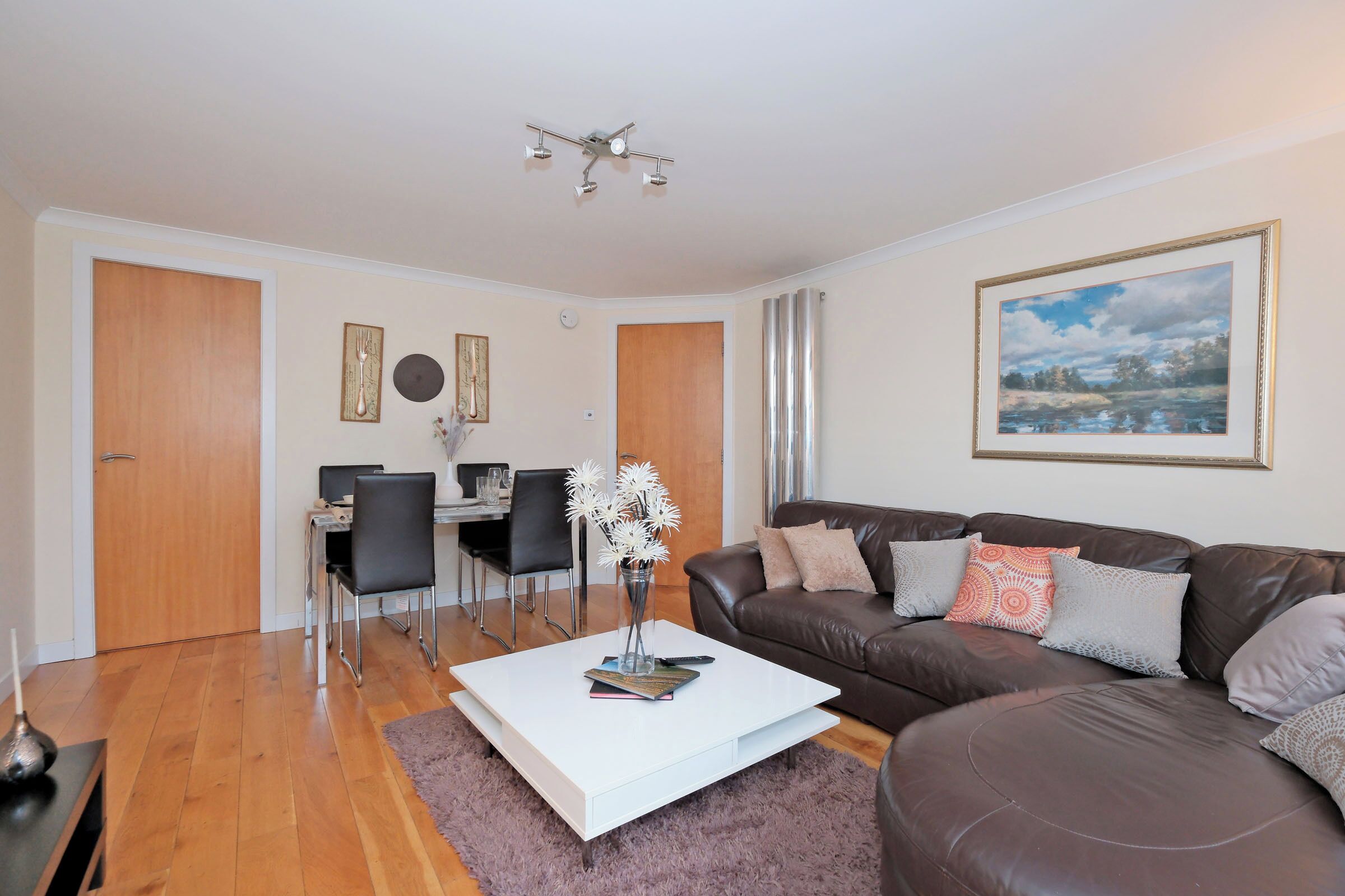 A modern living room with a white coffee table, a brown leather sofa, and a dining area with a table and chairs.